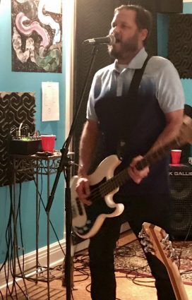 Will Styne plays bass with a graphic of R.E.M.’s “Reckoning” on the wall behind him.